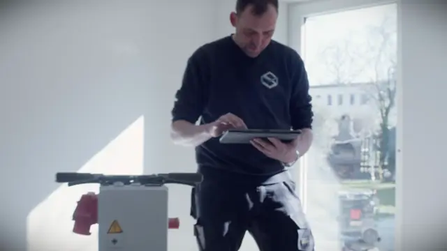 Monteur prüft den leeren Raum und hält den Bodenaufbau auf dem Tablet fest.